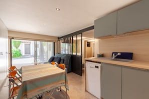 A compact kitchen with a dishwasher, a dining table with chairs, and a sofa.