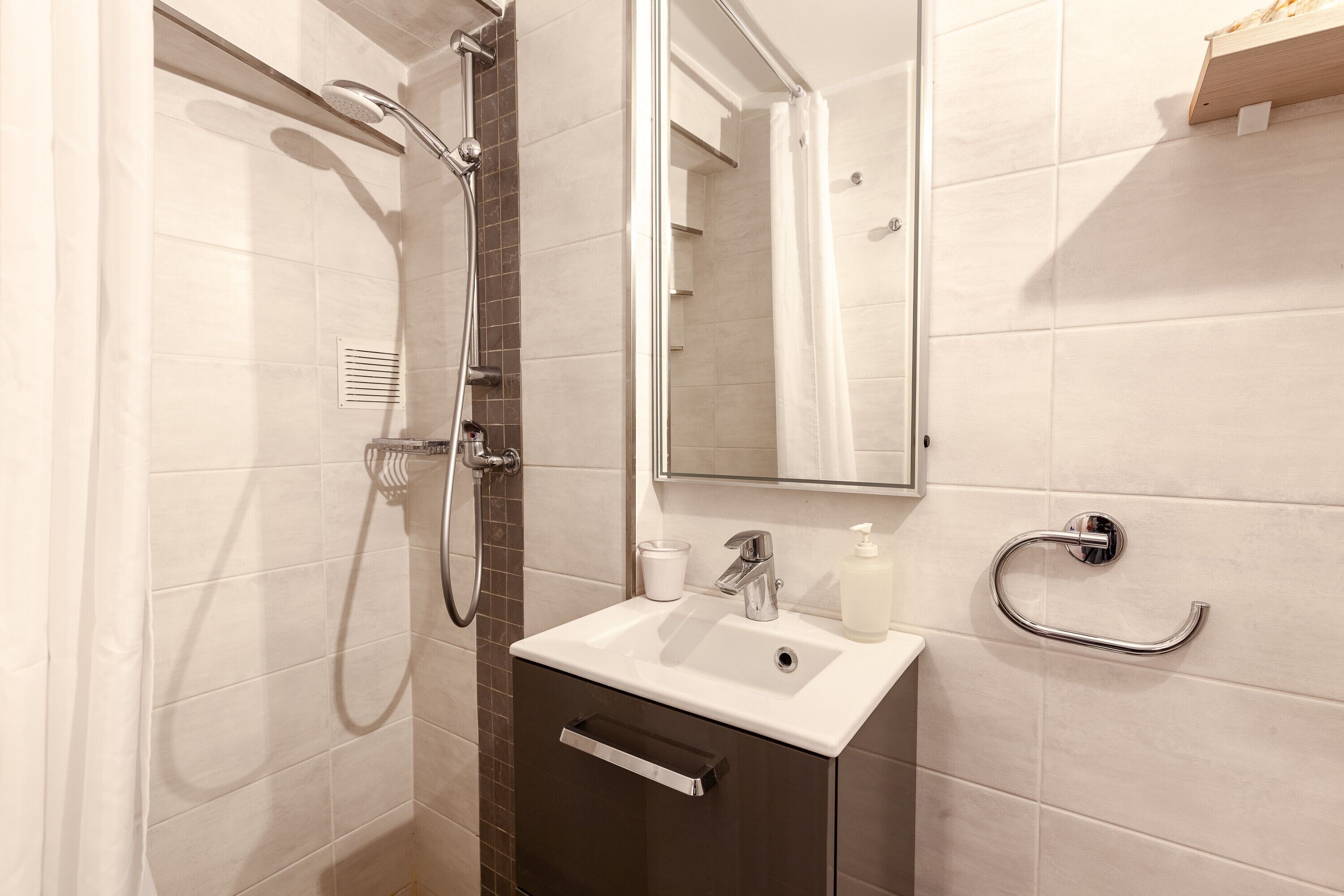 A bathroom with a shower, sink, mirror, and towel rack.