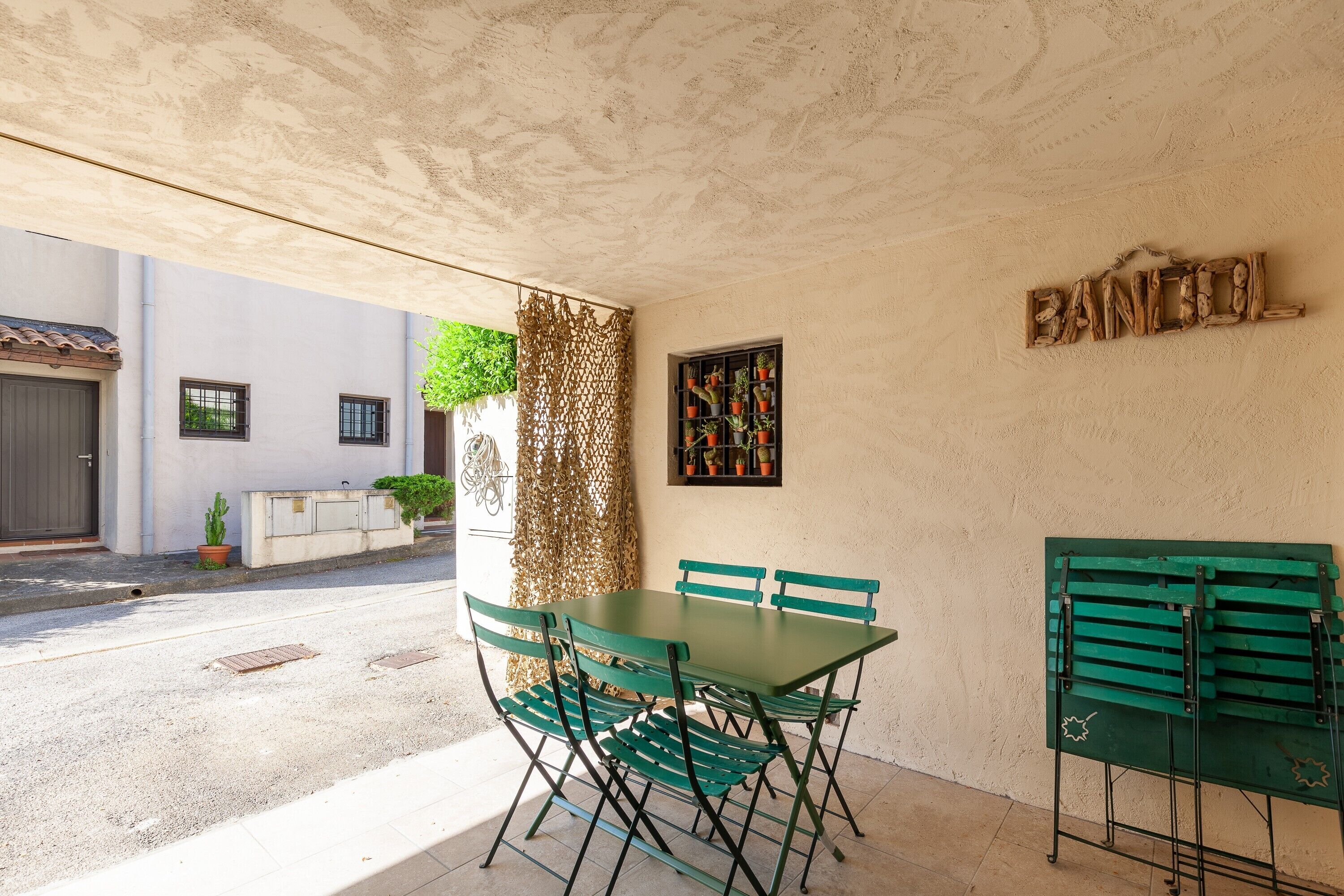 A covered outdoor dining area with a table and chairs, a decorative wall, and a small garden.