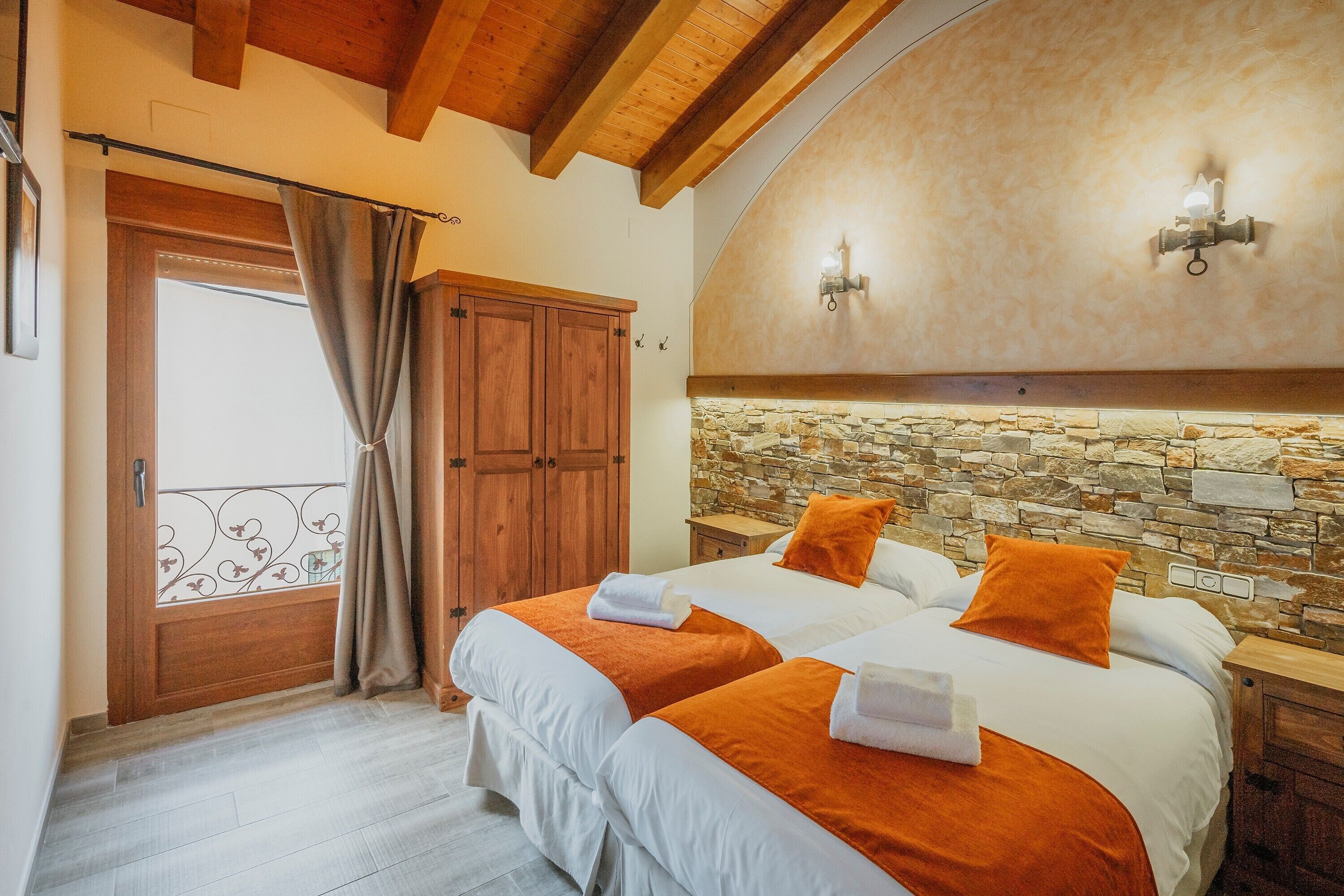 Un dormitorio con dos camas, una pared de piedra, vigas de madera en el techo y una puerta con cortina.