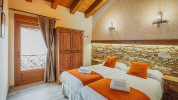 Un dormitorio con dos camas, una pared de piedra, vigas de madera en el techo y una puerta con cortina.