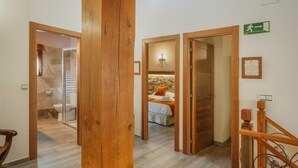 A hotel hallway with wooden doors, a staircase, and a bed with an orange pillow.