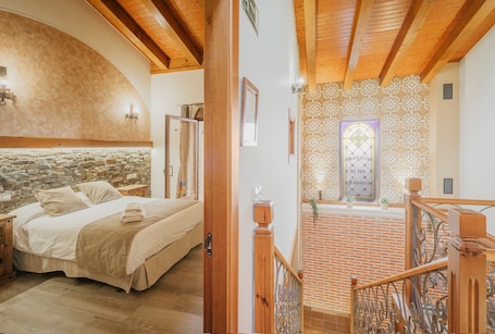 A bedroom with a stone wall, wooden ceiling beams, a bed, and a staircase leading to a lower level.. El Señorio De Los Fonseca: Country House with Pool, 5 Bedrooms in Coca, Segovia