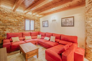 Un accogliente soggiorno con un divano a divano rosso, un tavolino in legno, pareti in pietra e travi di legno al soffitto.