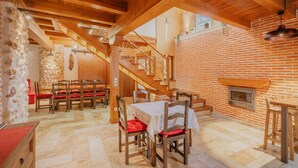 A dining area with wooden tables and chairs, a brick wall with a fireplace, and a staircase leading to an upper level.