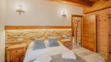 Un dormitorio con pared de piedra, cabecero de madera, dos mesitas de noche, una cama con almohadas y un armario de madera.