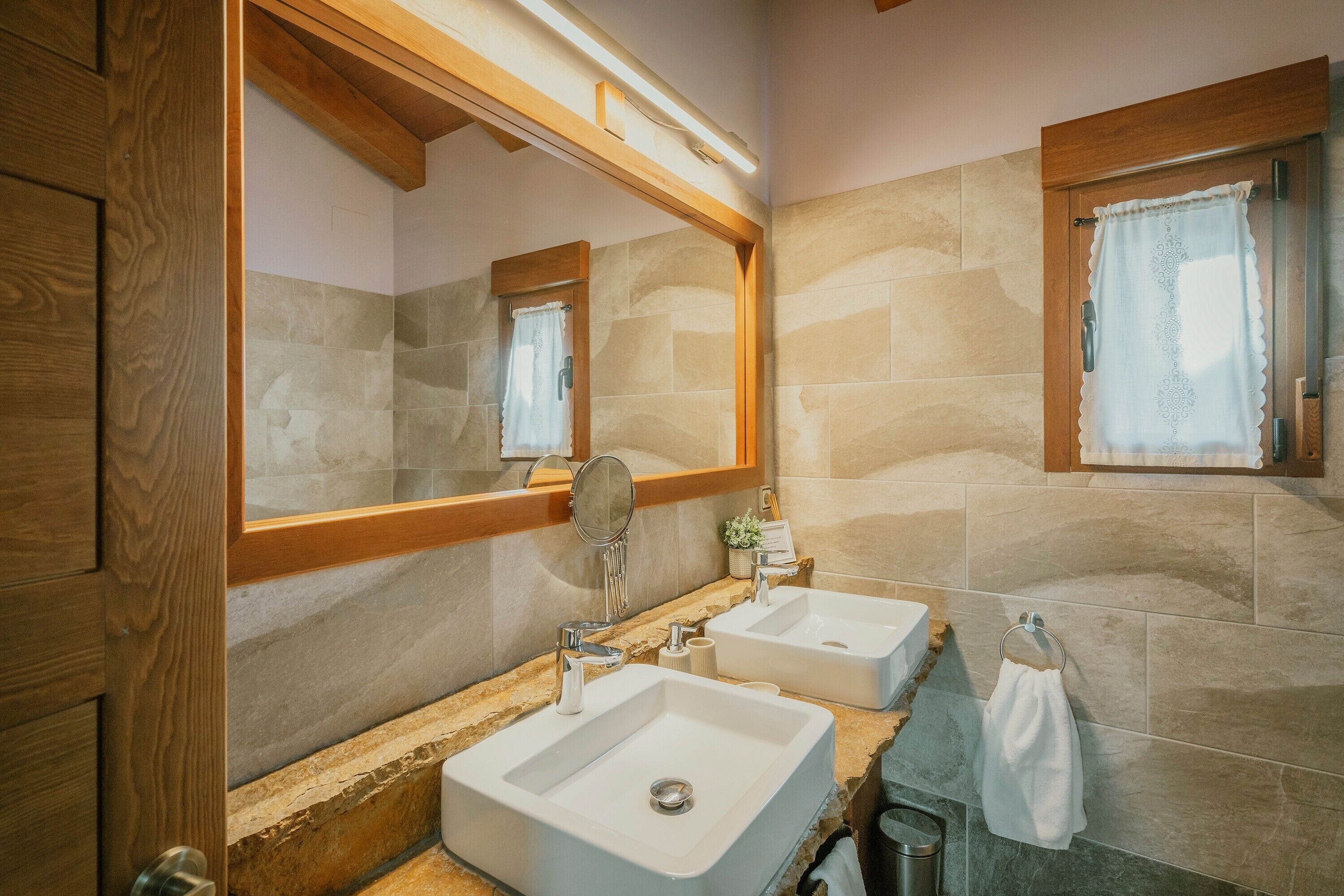 A bathroom with two sinks, a mirror, and a window with a curtain.