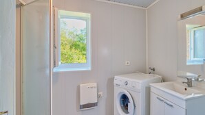 A compact, modern bathroom with a built-in washing machine, a small window with a view of greenery, and a mirror above the sink. - Charming Holiday Home Quiétude in Meyrals (Meyrals)