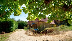 A stone house with a gravel driveway, surrounded by greenery and a clear sky. - Charming Holiday Home Quiétude in Meyrals (Meyrals)