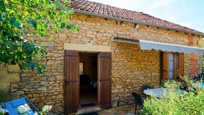 A stone building with a tiled roof, a wooden door, and a small outdoor seating area with a table and chairs. - Charming Holiday Home Quiétude in Meyrals (Meyrals)