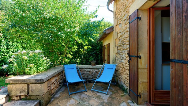 A stone building with a wooden door, a stone wall, and a garden with a bench. - Charming Holiday Home Quiétude in Meyrals (Meyrals)