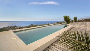 A rectangular swimming pool with a clear blue edge, surrounded by a wooden deck and palm trees, overlooking a coastal landscape. - 'Casa Del Cielo' with Sea View, Private Pool and Wi-Fi (Adeje)
