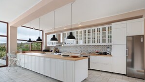 Een moderne keuken met witte kasten, een groot eiland, zwarte hanglampen en een roestvrijstalen koelkast.