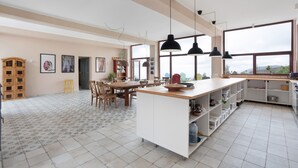 Een ruime keuken met een groot eiland, hanglampen en uitzicht door grote ramen.