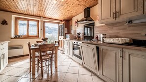 Une cuisine avec un plafond en bois, des armoires blanches, une table à manger avec des chaises et une vue par la fenêtre.