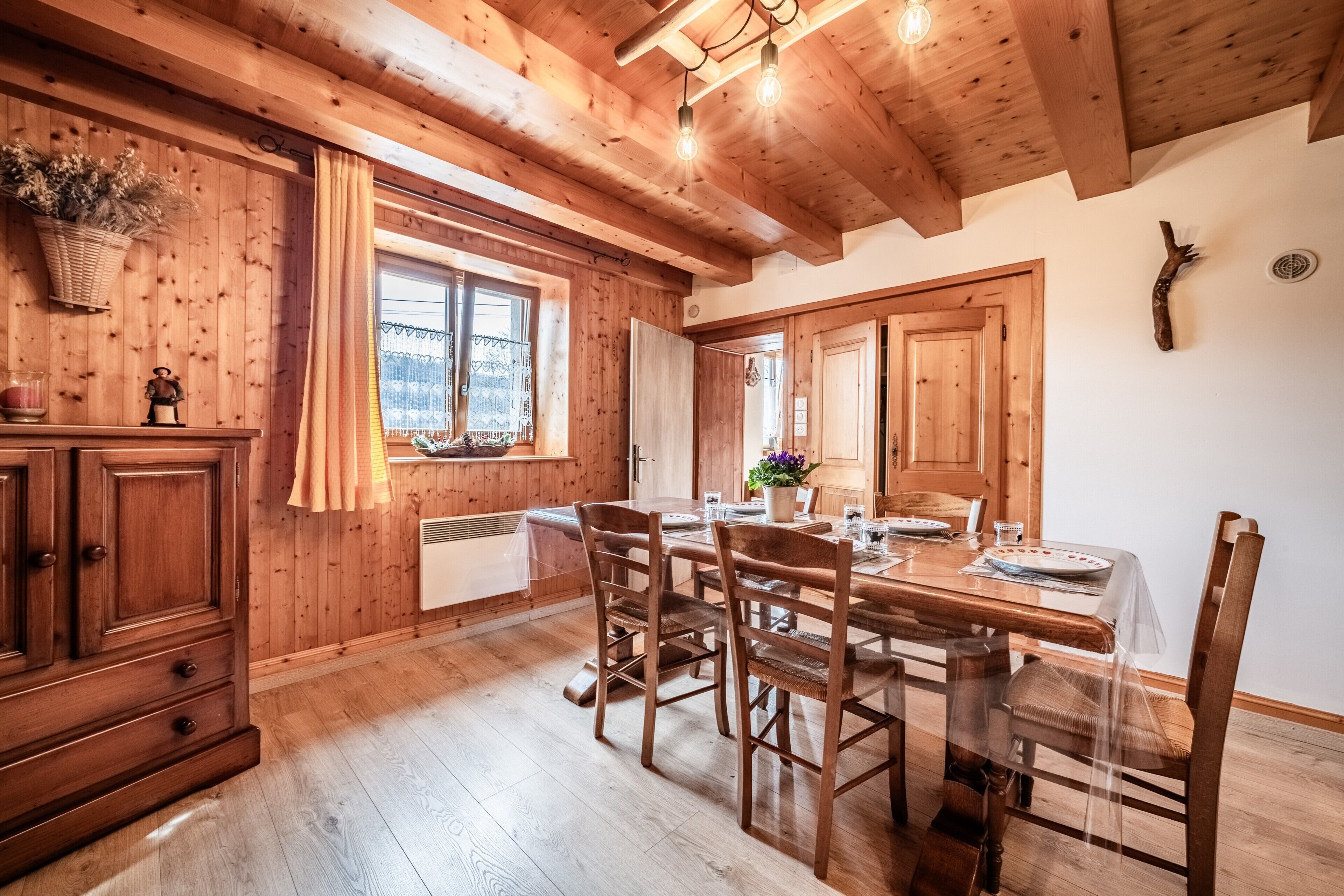 Un intérieur en bois comprenant une table à manger, des chaises, un buffet et une fenêtre avec des rideaux.