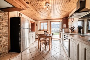 A kitchen with a wooden ceiling, stone wall, and a view of a snowy landscape.