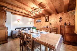 A wooden interior with a dining table set for four, a sofa, and a clock on the wall.