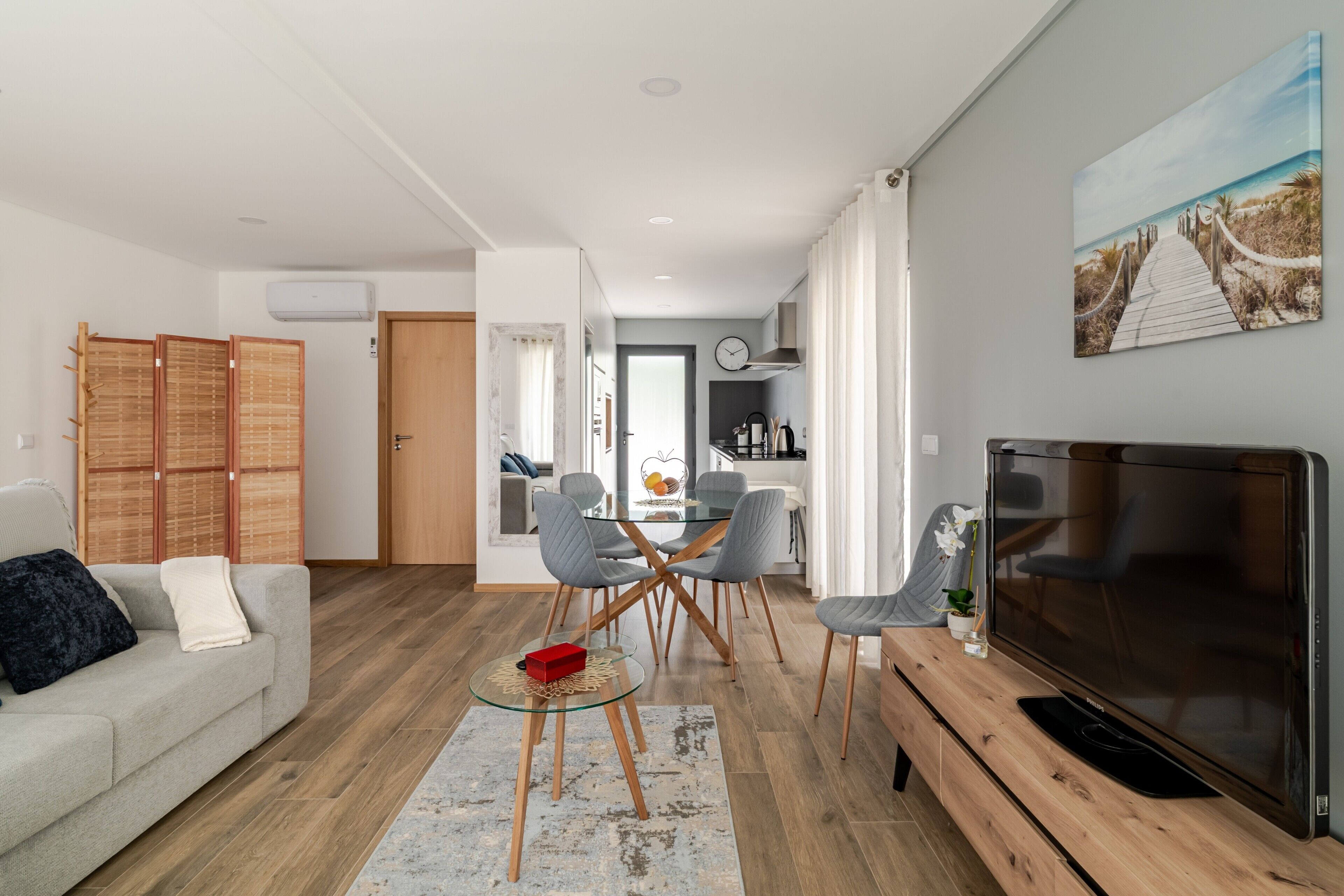 A modern living room with a sofa, a glass coffee table, a TV, and a dining area with chairs and a table.