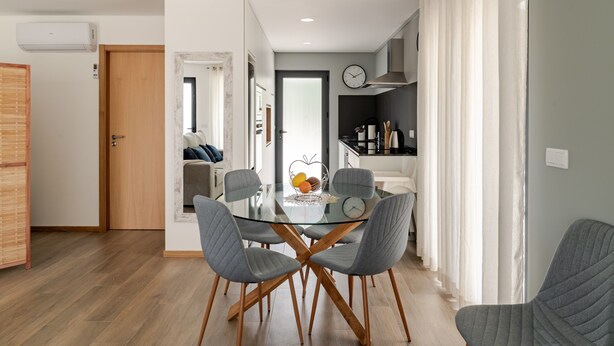 Una cocina moderna con una mesa de comedor de cristal, sillas tapizadas en gris y un reloj visible en la pared.