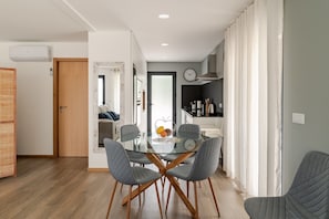 Une cuisine moderne avec une table à manger en verre, des chaises à revêtement gris et une horloge visible au mur.