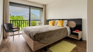 Un dormitorio con cama, una silla, una mesita de noche y vistas a zonas verdes y una montaña.