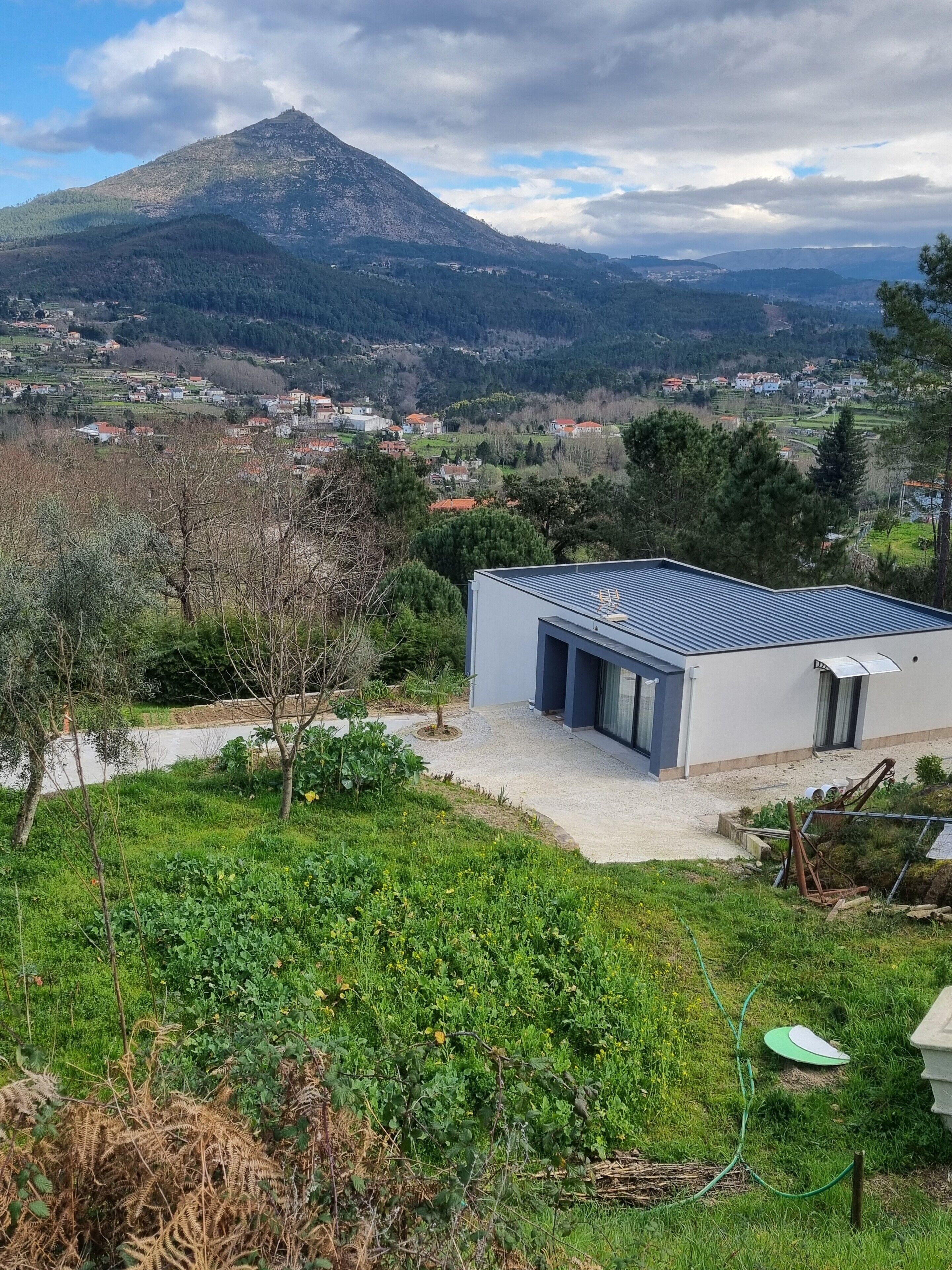 A modern building with a flat roof, surrounded by greenery and a mountainous backdrop.