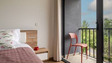 Ein Schlafzimmer mit Bett, Nachttisch, Sessel und einem Balkon mit Blick auf Bäume.