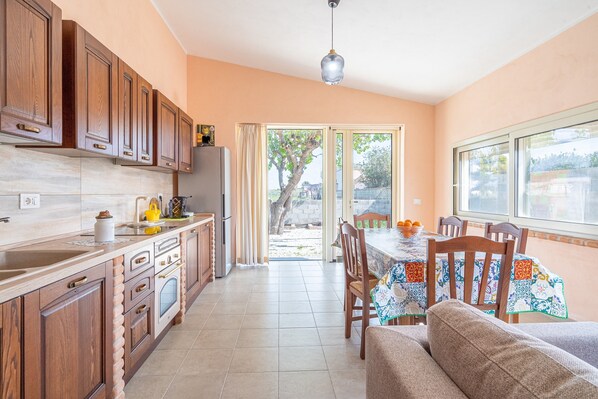 A kitchen with wooden cabinets, a dining table with chairs, and a view through a glass door to the outside.
