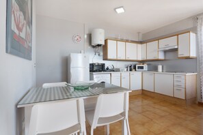 A modern kitchen with white cabinets, a microwave, a kettle, and a glass-top table with chairs. - Vacation 'Dorado Atardecer Beach Sand' with Sea View, Shared Pool and Wi-Fi (Puerto de Santiago)