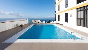 Una piscina en la azotea con vistas despejadas al océano, paredes blancas y detalles en amarillo.