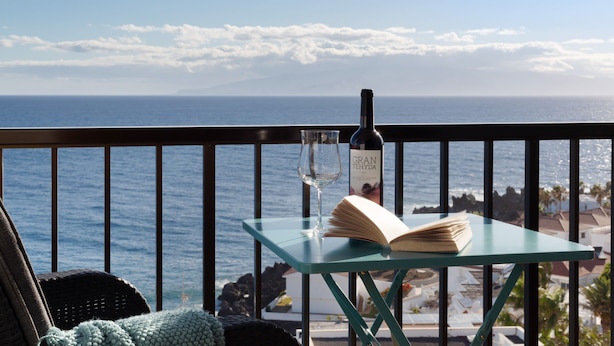 Un balcón con una mesa, una botella de vino y una copa, con vistas al océano.