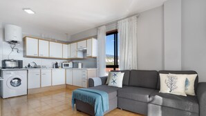 Una sala de estar moderna con un sofá gris, una manta azul y vistas a la montaña a través de un ventanal grande.