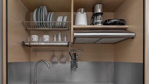 Eine kleine Küche mit Spüle, Herd und Regalen für Geschirr und Besteck.