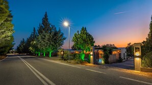 Eine gut beleuchtete Straße im Dämmerlicht mit einem verschlossenen Eingang, Bäumen und wolkenlosem Himmel.