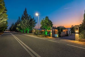 A well-lit street at dusk with a gated entrance, trees, and a clear sky.