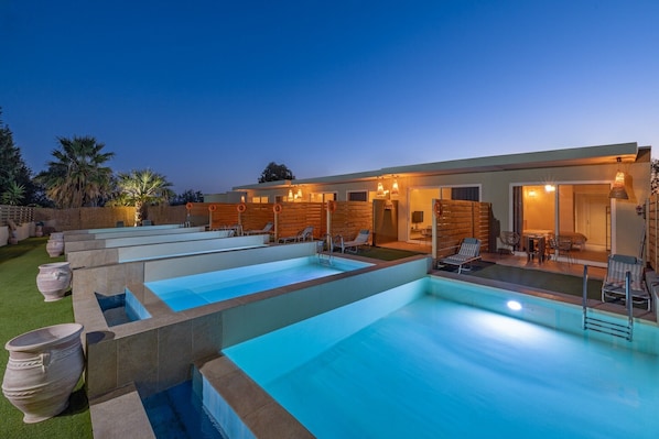 Un espace piscine comprenant plusieurs piscines, des chaises longues et un bâtiment aux murs en bois et aux portes en verre.