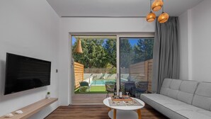 Una sala de estar moderna con una televisión de pantalla plana, un sofá, una mesa de comedor y vista a un patio trasero con piscina.