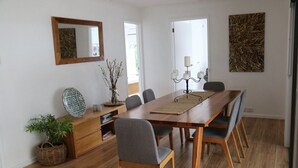 Ein Essbereich mit einem Holztisch, sechs grauen Stühlen, einer gewebten Tischmatte, einem Kerzenleuchter und einem Spiegel an der Wand.