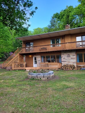 Une cabane en bois à deux étages, dotée d’un balcon, d’une cheminée en pierre et d’une pelouse bien entretenue.
