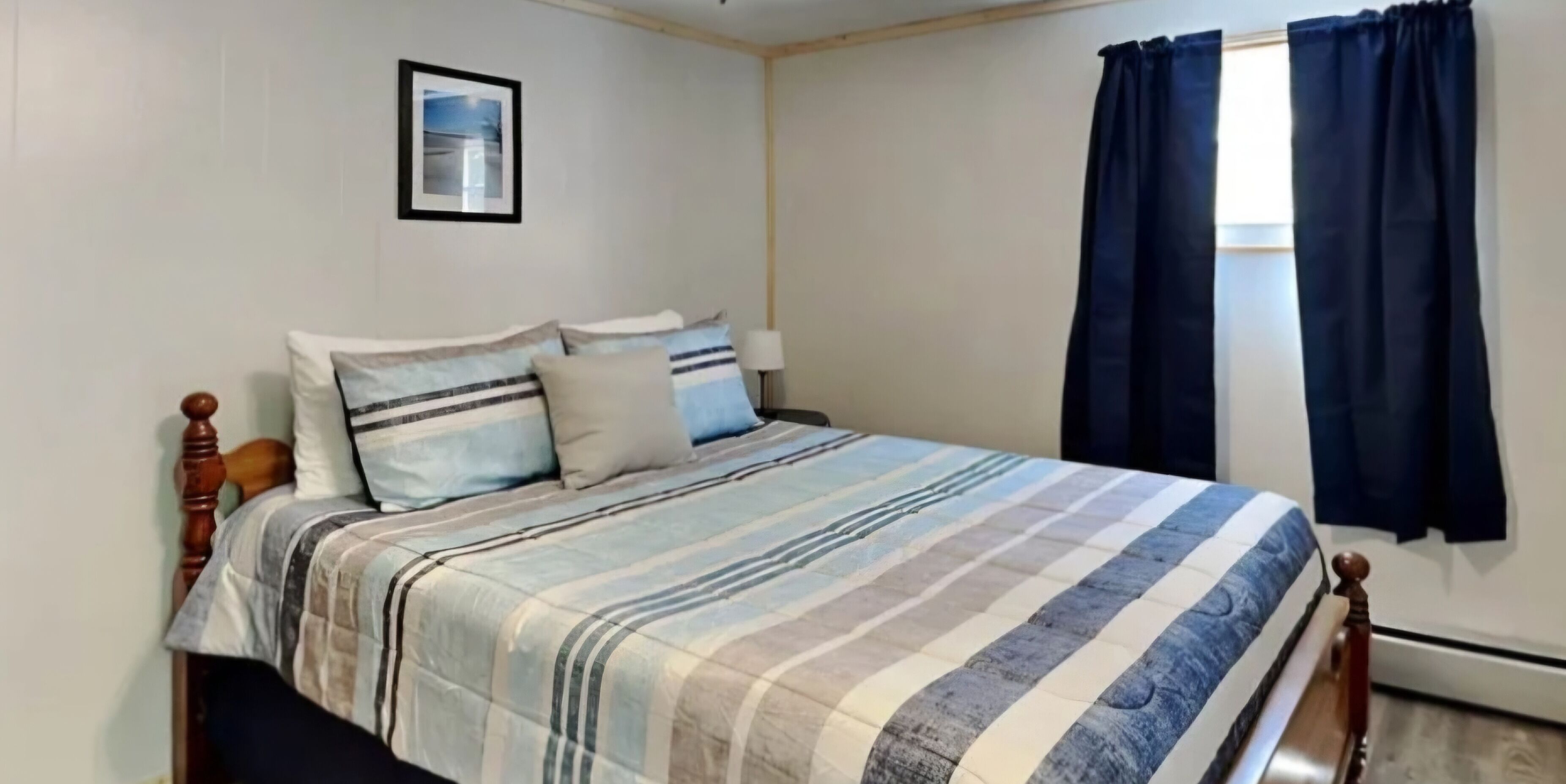 A bedroom with a bed, a nightstand, a framed picture on the wall, and a window with curtains.