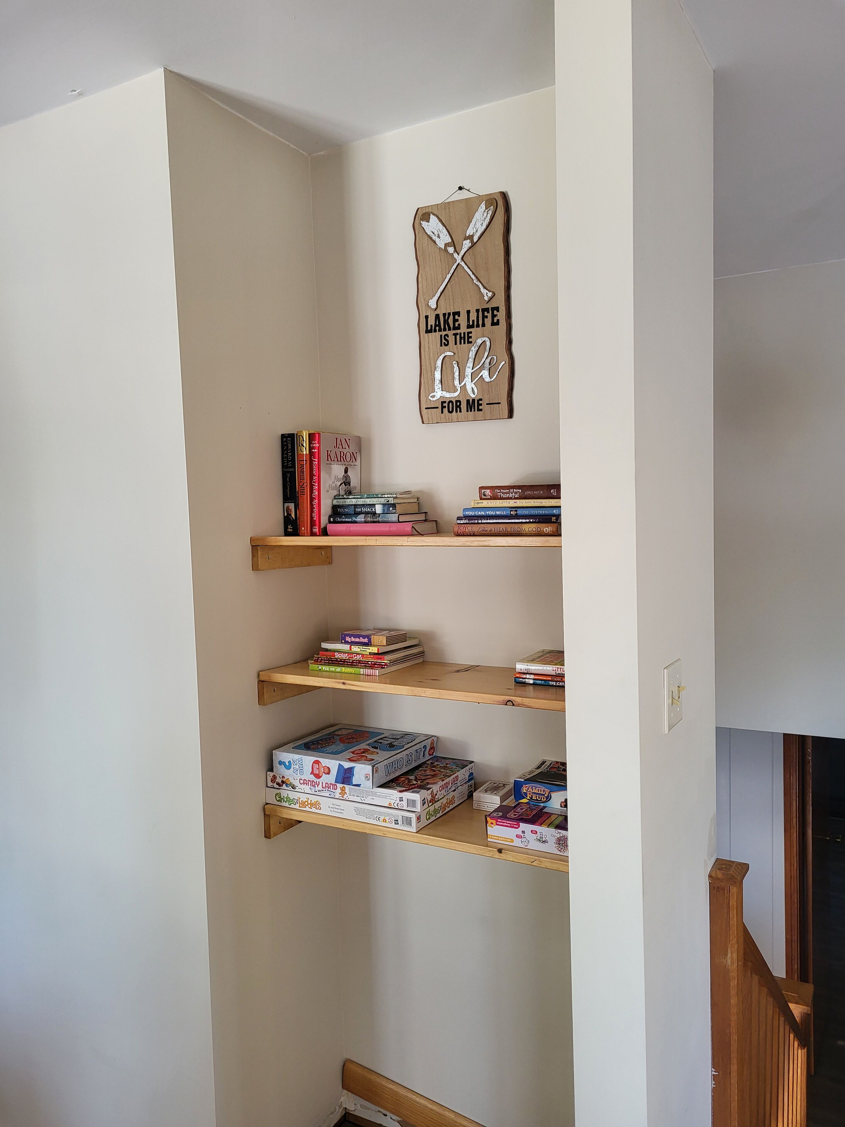A corner of a room with a wooden bookshelf containing books and board games.