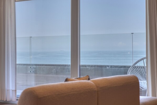 A room with a large window overlooking the sea, a white chair, and a view of the ocean. - Apartment 3BD Praia Porto Matosinhos (Matosinhos)