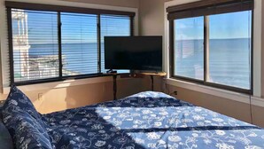 A bedroom with a bed, a TV on a stand, and large windows with a view of the sea. - 3 bedroom, waterfront cottage on the shores of the Chesapeake Bay. (North Beach)