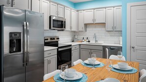 Una cocina moderna con armarios blancos, electrodomésticos de acero inoxidable y una mesa de comedor de madera para cuatro.