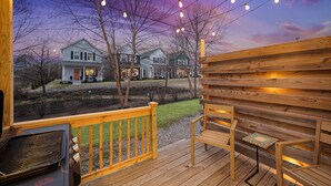 A wooden deck with a grill and chairs, overlooking a row of houses under string lights. - Cozy 3BR/2.5BA Retreat in Nashville/Old Hickory, 20min to Downtown & Airport (Nashville)