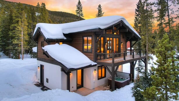 Een houten blokhut met een balkon en een hottub, omgeven door sneeuw en bomen.