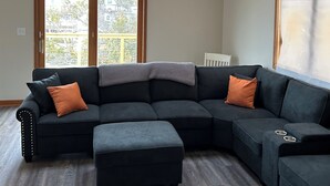 En moderne stue med en hjørnesofa, loftventilator og store vinduer.