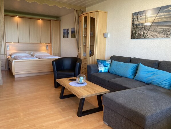 A cozy room with a bed, a sofa, a chair, and a table. There is a cabinet with glass doors and a painting on the wall.