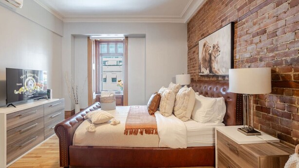Ein Schlafzimmer mit einem großen Bett, einem Fernseher, einer Ziegelwand und einem Fenster.